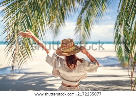 Summer beach vacation concept, Happy woman with hat relaxing at the seaside and looking away, in the summer against a backdrop of palm trees and sea beach. Royalty-Free Stock Photo #2172255077