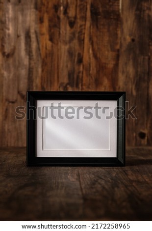 blank black photo frame on wood table and wall witn sunlight from window