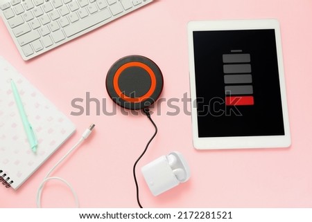 Wireless charger pad, uncharged tablet computer and stationery supplies on color background