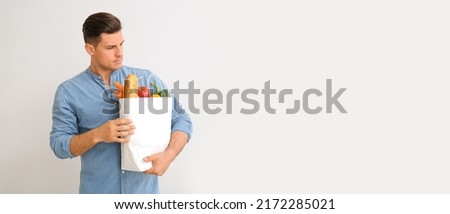 Young man with paper bag full of food on light background with space for text