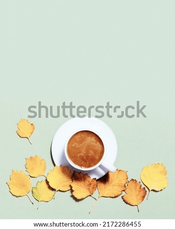 Cup of coffee with milk and red yellow autumn leaves on pastel green paper background. Autumn, fall composition, flat lay, top view, copy space