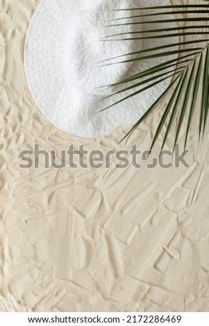 Summer minimal background, top view wide-brimmed sun hat under palm leaf on natural sand beach. Summer aesthetic photography pastel beige colored, copy space, vacation, relaxation concept. Above view
