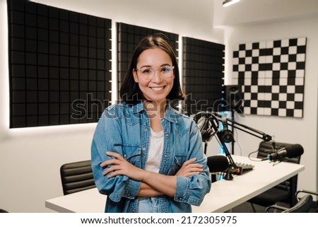 Beautiful happy young female radio host smiling while broadcasting in studio