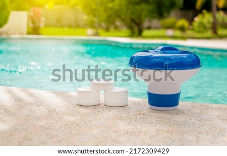 A pool float and chlorine tablets on the edge of a swimming pool. Tablets with chlorine dispenser for swimming pools. Chlorine tablets with dosing float, Pool float and chlorine tablets Royalty-Free Stock Photo #2172309429