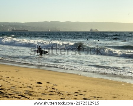 Surfer silhouette on the beach at sunset with cargo ships by Valparaiso harbor on background in Chile. Summer water sport concept