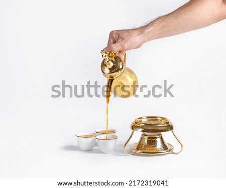 An Arab man in white Kandura serving arabic coffee and Dalah Royalty-Free Stock Photo #2172319041