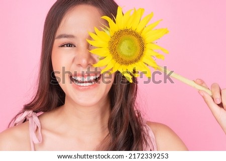 Asian teenager girl holding sunflower cover own eye on pink background. Close up happy young woman long hair casual use fresh sunflower close eyes smiling face toothy over isolated. Lifestyle