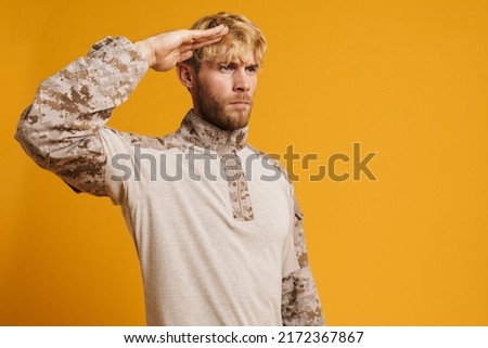 European military man wearing uniform saluting while looking aside isolated over yellow background