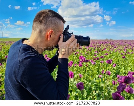 attractive man standing in violet poppy field. boy taking photos in nature. photograph 