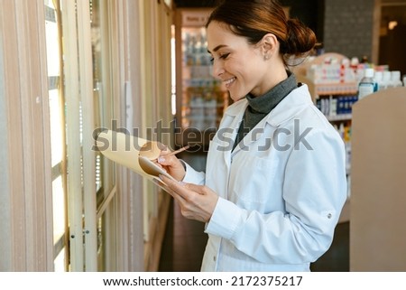 White pharmacist woman wearing medicine coat smiling while working in apothecary