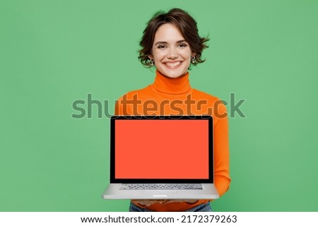 Young smiling happy woman 20s wear casual orange turtleneck hold use work on laptop pc computer with blank screen workspace area isolated on plain pastel light green color background studio portrait.