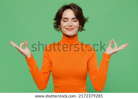 Young smiling woman 20s wear casual orange turtleneck hold spreading hands in yoga om aum gesture relax meditate try to calm down isolated on plain pastel light green color background studio portrait. Royalty-Free Stock Photo #2172379281