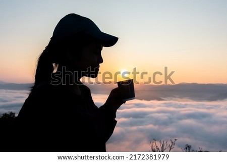 Picture of a woman drinking coffee on top of a mountain at sunrise.