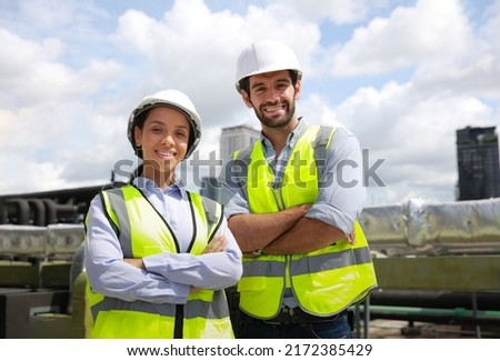 Portrait diversity male and female engineer work together on roof top of site line . Portrait of engineer with green safety vest and white hard hat at building site looking at camera  Royalty-Free Stock Photo #2172385429