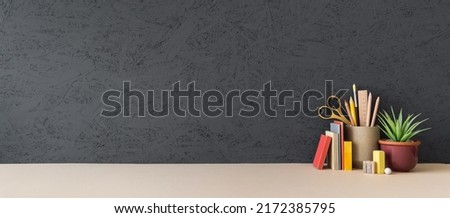 Creative desk with a blank picture frame or poster, desk objects, office supplies, books, and plant on a dark matte grey background.