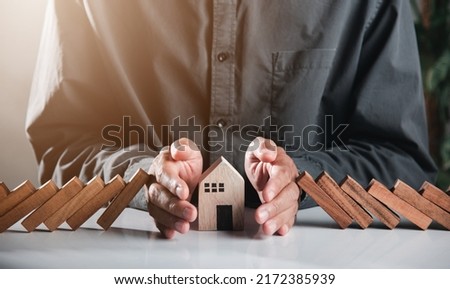 Business risk plan real estate protection. Man hand blocks wood block from many row falling wooden block like domino to house model, Insurance ideas to prevent loss concept Royalty-Free Stock Photo #2172385939
