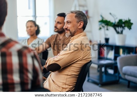 A focused mature man follows the flow of the story, sitting and listening to the others during the group therapy.