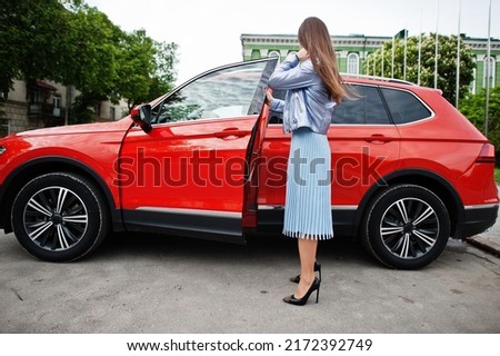 Outdoor photo of gorgeous woman posing near orange suv car.