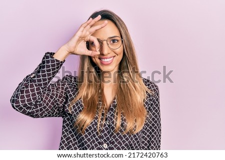 Beautiful hispanic woman wearing casual clothes and glasses smiling happy doing ok sign with hand on eye looking through fingers 
