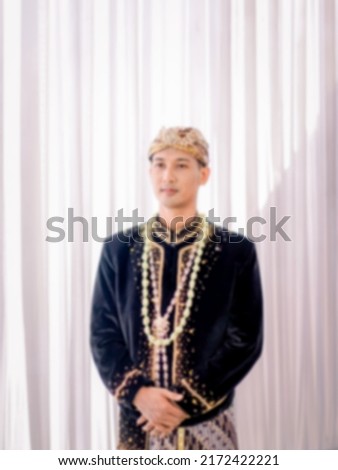 photo blur The groom wears Javanese traditional clothes, black and blangkon clothes and a jasmine necklace at his wedding. Beskap is a traditional heritage clothing from Java, Indonesia