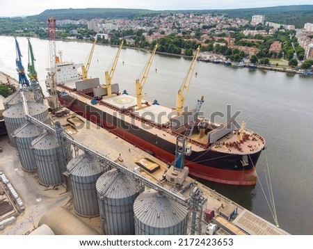 Loading grain into holds of sea cargo vessel in seaport from silos of grain storage. Bunkering of dry cargo ship with grain. Aerial top view Royalty-Free Stock Photo #2172423653