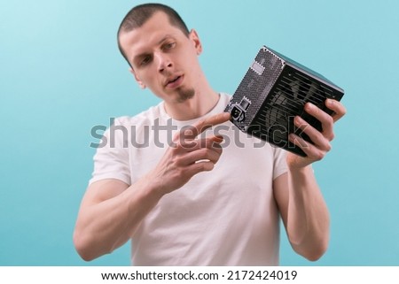 A man shows with a pointing finger at a connector of a computer power supply on a blue background. Hand. Electricity. Electronic. Supply. Component. Connection. Hardware. Unit. Electric