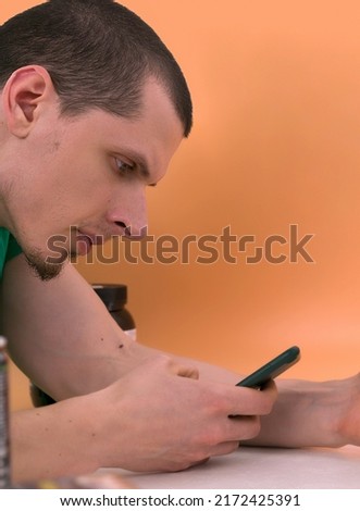 The man focused on his phone on a yellow background. Looking. Cellular. Sitting. App. Male. Sms. Browsing. Lifestyle. Game. Browse. Attractive. Connection. Look. Content