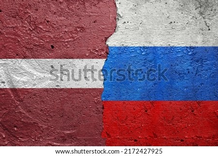 Latvia and Russia - Cracked concrete wall painted with a Latvian flag on the left and a Russian flag on the right