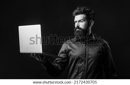 Bearded male businessman holding a computer in his hands isolated on black background. Businessman using his laptop, pc. Black and white.