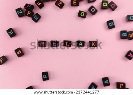 Relax button concept. Black beads on trendy pink background making word. Lifestyle phrase made of small letters symbolizing relax and keep calm