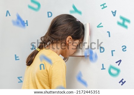 Sad and tired caucasian girl with dyslexia holds a book on her forehead. Flying tangled letters in the air. The child learns to speak and read correctly