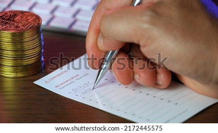 A closeup view of a man writing his secret cryptocurrency wallet recovery "seed" phrase on a note card.  	 Royalty-Free Stock Photo #2172445575