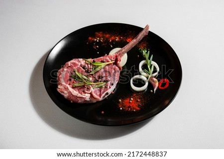 Raw pork meat on the bone with peas, paprika, chili, salt, rosemary, onions, garlic in a plate on a white background