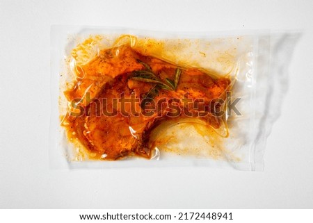 Vacuum packed raw marinated meat with rosemary on a white background