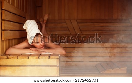 Young woman relaxing and sweating in hot sauna wrapped in towel. Girl In Sauna. Interior of Finnish sauna, classic wooden sauna with hot steam. Russian bathroom. Relax in hot bathhouse with steam. Royalty-Free Stock Photo #2172452901