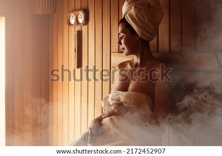 Young woman relaxing and sweating in hot sauna wrapped in towel. Girl In Sauna. Interior of Finnish sauna, classic wooden sauna with hot steam. Russian bathroom. Relax in hot bathhouse with steam. Royalty-Free Stock Photo #2172452907