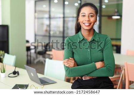 Successful young african-american female entrepreneur, small business owner, female office employee, black businesswoman wearing green casual shirt stands in confident pose with arms crossed Royalty-Free Stock Photo #2172458647
