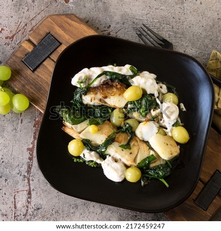 a plate of fried halibut with spinach and grapes on the table