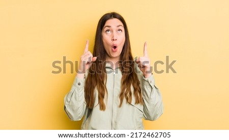 pretty caucasian woman feeling awed and open mouthed pointing upwards with a shocked and surprised look