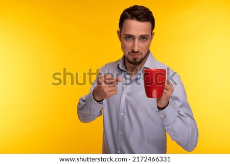 A guy in a blue shirt holds a red cup in his hand and points to it