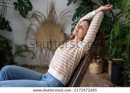 No stress. Serene young Polish girl resting in tropical indoor garden, peaceful Italian female relaxing with closed eyes, stretching arms, enjoying peace in tropical oasis of urban jungle interior Royalty-Free Stock Photo #2172472685