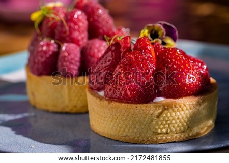 Cupcake with flower petals, strawberries, raspberries and cream in a plate on a wooden table