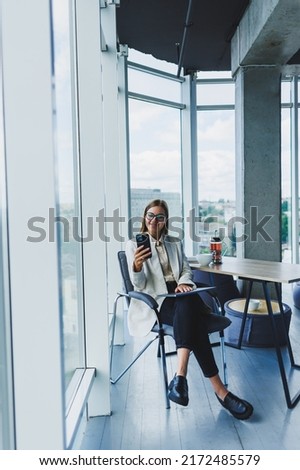 Attractive female blogger in a jacket with a modern smartphone in her hands, thoughtful and daydreaming, a young blogger holding a mobile phone, reflects on social media posts