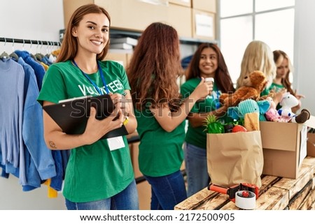 Group of young volunteers woman working at charity center. Girl smiling happy writing on clipboard. Royalty-Free Stock Photo #2172500905
