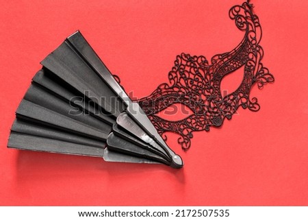 Black lacy mask and folding hand fan on red background Royalty-Free Stock Photo #2172507535