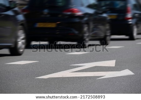 Dark cars drive one after the other in a lane on an asphalt street. The right lane with arrows straight ahead and to the right is empty. Focus on the arrows