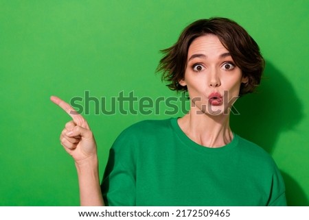 Photo of shocked funky woman wear casual t-shirt pointing empty space isolated green color background