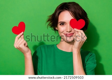 Photo of adorable funky young lady dressed casual t-shirt red heart cover eye isolated green color background