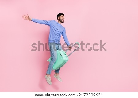 Full length photo of excited pretty arabian man wear long sleeve shirt riding suitcase jumping empty space isolated pink color background Royalty-Free Stock Photo #2172509631