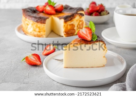A piece of Basque burnt cheesecake or San Sebastian cheesecake with fresh strawberries on a white plate on a gray background. Selective focus. Copy space Royalty-Free Stock Photo #2172523621